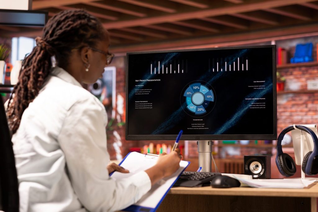 Woman looking at Sales Statics on Computer taking notes